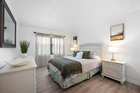 A bedroom with a bed, nightstand, and a plant on the dresser.