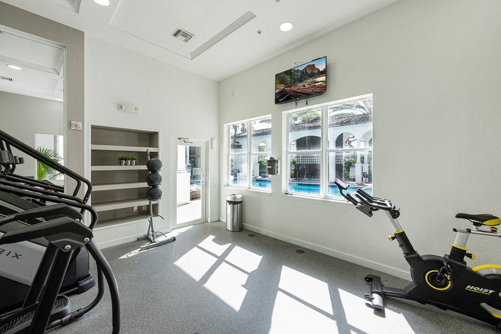 A gym with a treadmill, exercise bike and windows.
