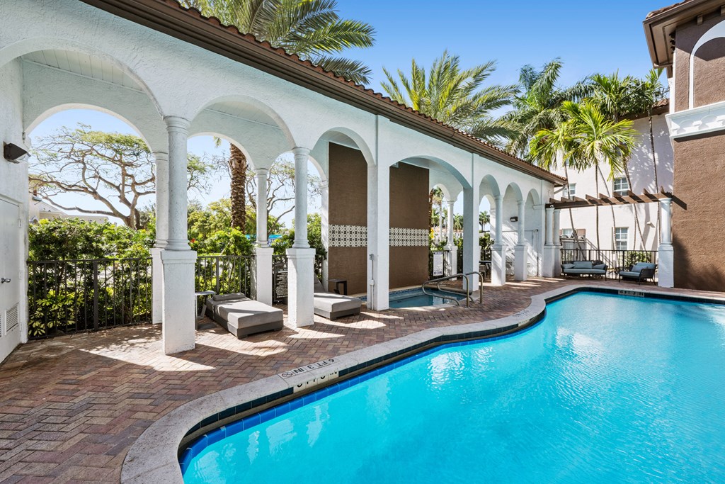 A pool surrounded by arches and palm trees.