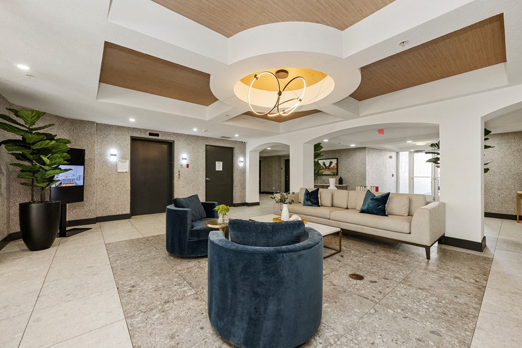 A spacious lobby with a blue velvet ottoman and a white sofa.
