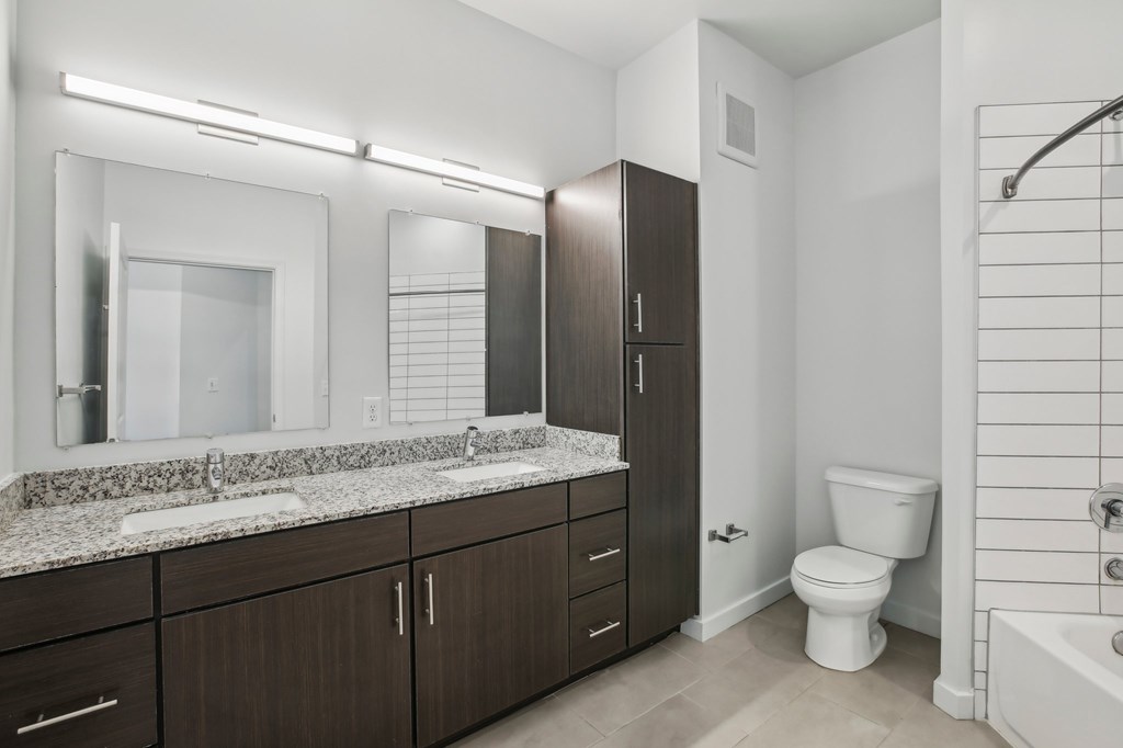 A modern bathroom with a marble countertop and dark wood cabinets.