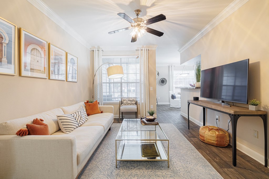 A living room with a white couch, a glass coffee table, and a television.