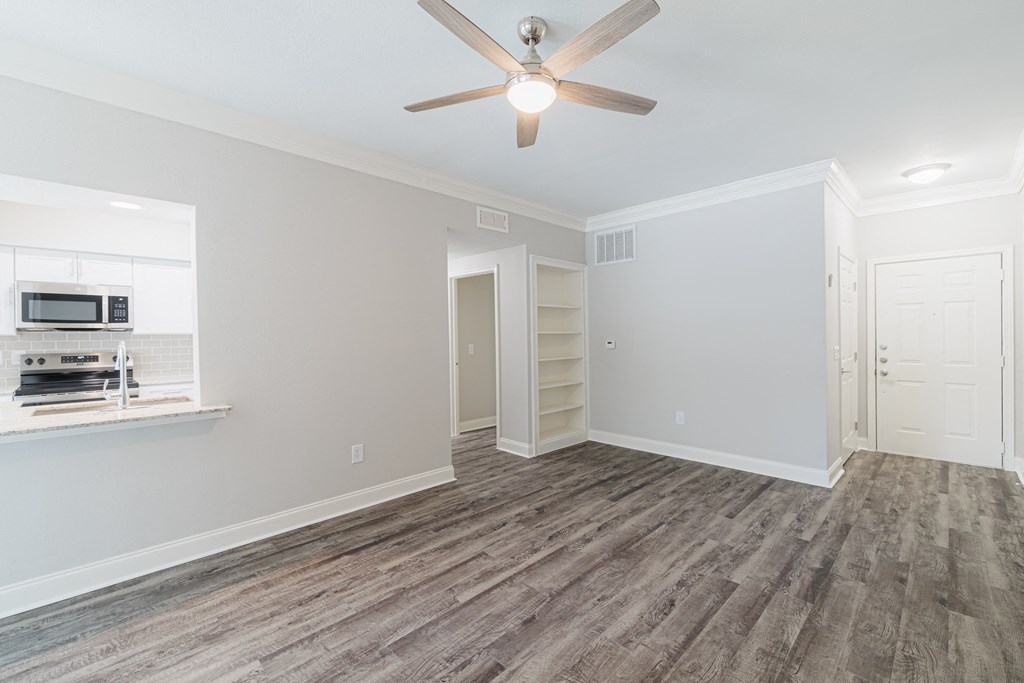 an empty living room with a ceiling fan and a kitchen