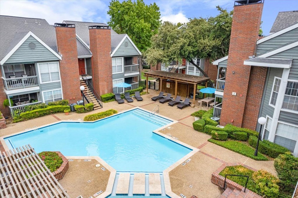 A large swimming pool surrounded by a patio area with chairs and a hot tub.