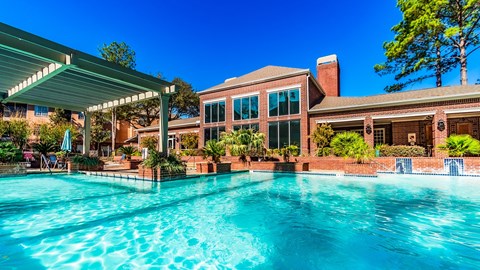 A large swimming pool in front of a house with a covered patio area.