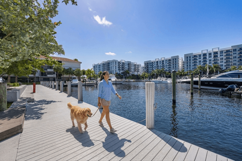 A woman walking her dog on a boardwalk by the water.