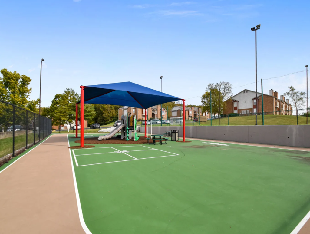 a basketball court with a playground and a blue canopy