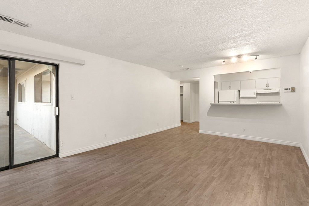the living room and dining room of an apartment with white walls and wood floors