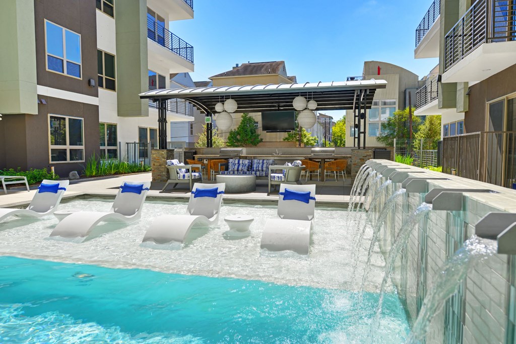 a pool with a waterfall and lounge chairs in front of a building