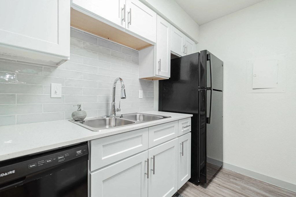 A kitchen with white cabinets and a black refrigerator.