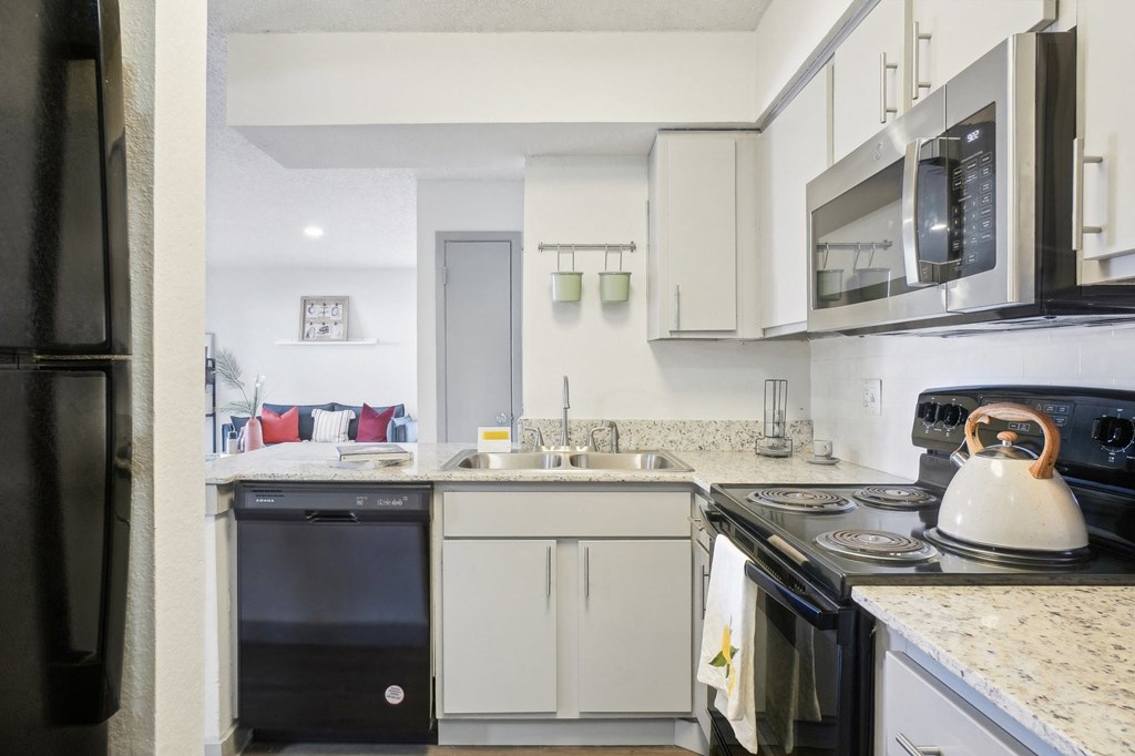 A black refrigerator is on the left of a kitchen with a black oven and a black dishwasher.