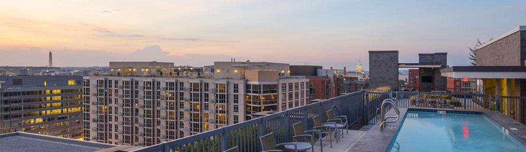 A rooftop pool with chairs and a cityscape in the background.