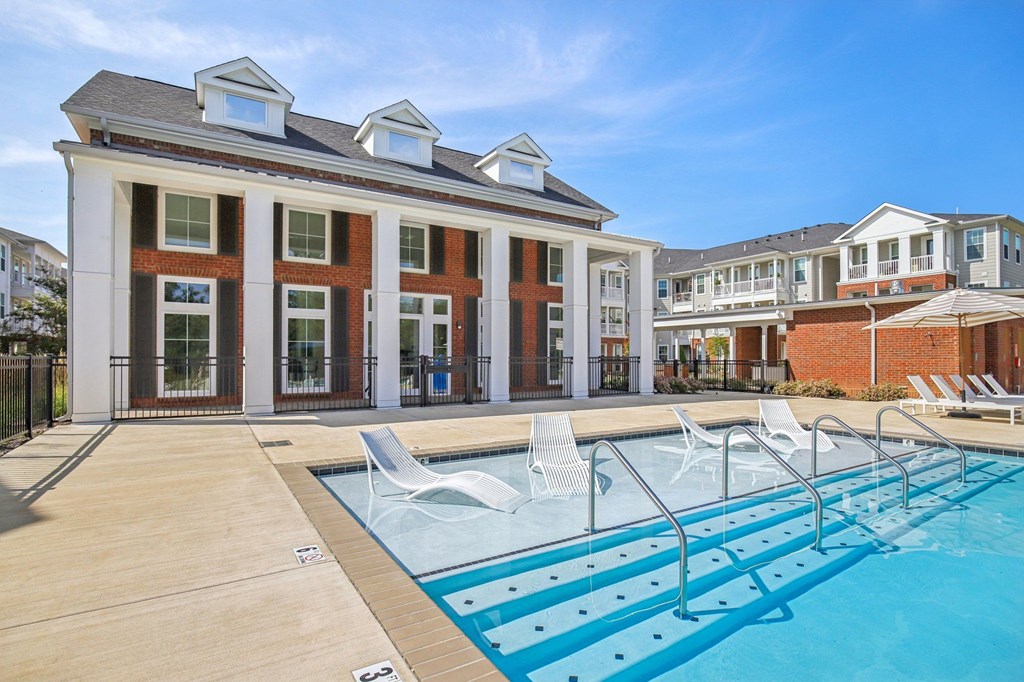 A pool area with a building and lounge chairs.