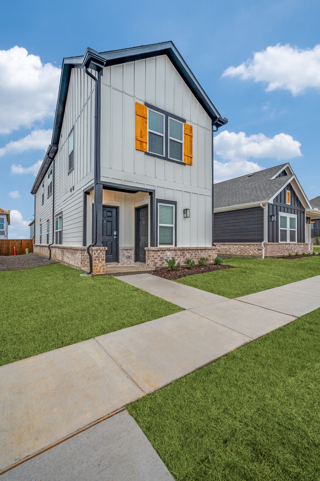 A modern house with a grey and white exterior and orange window shutters.