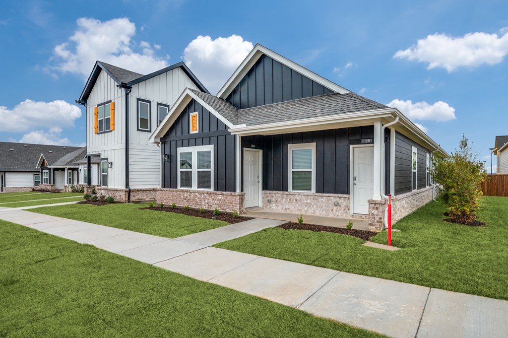 A modern house with a grey and black exterior and a red post in the front yard.