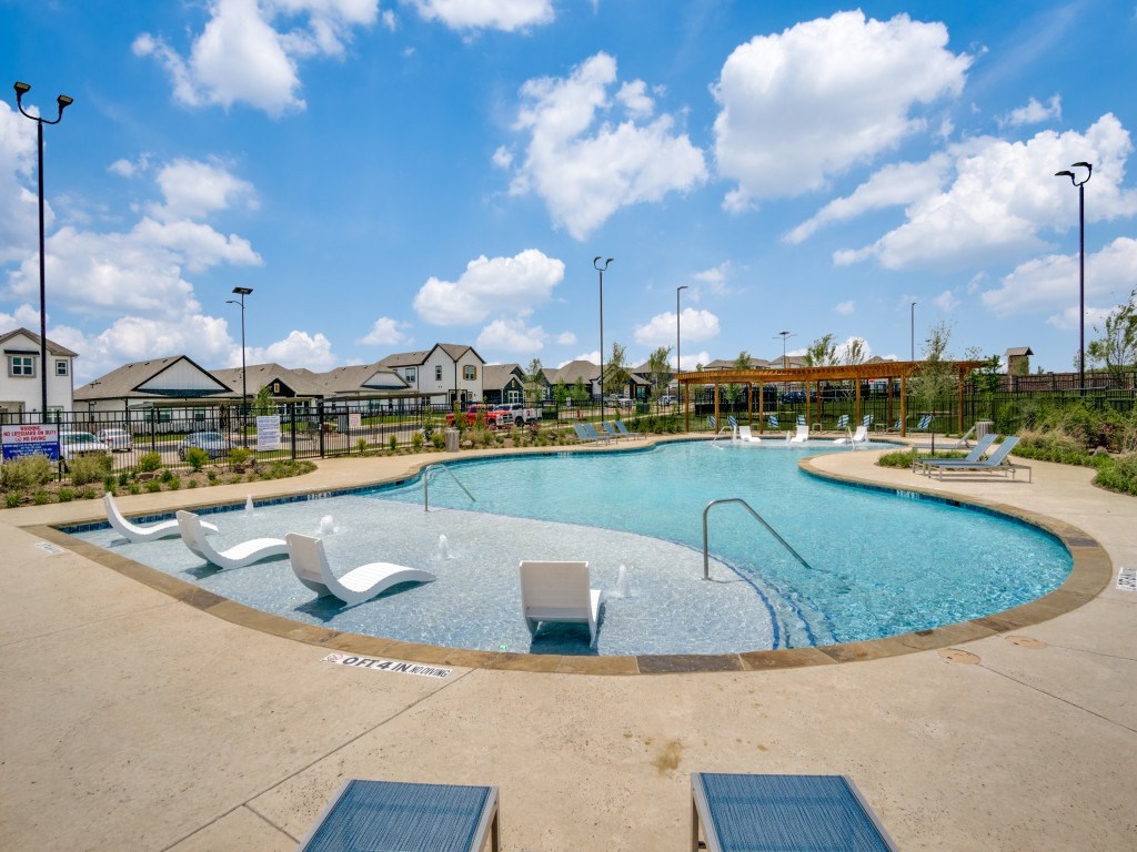 A round swimming pool with a blue tiled edge and white lounge chairs.
