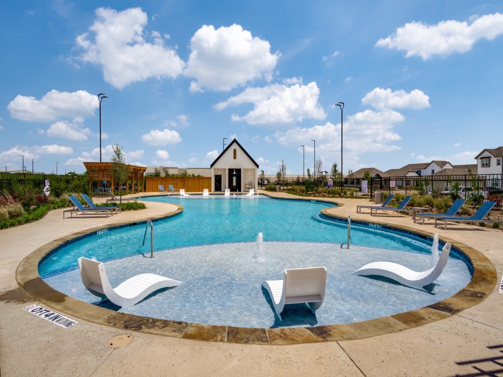 A round swimming pool with a fountain in the middle and lounge chairs around it.