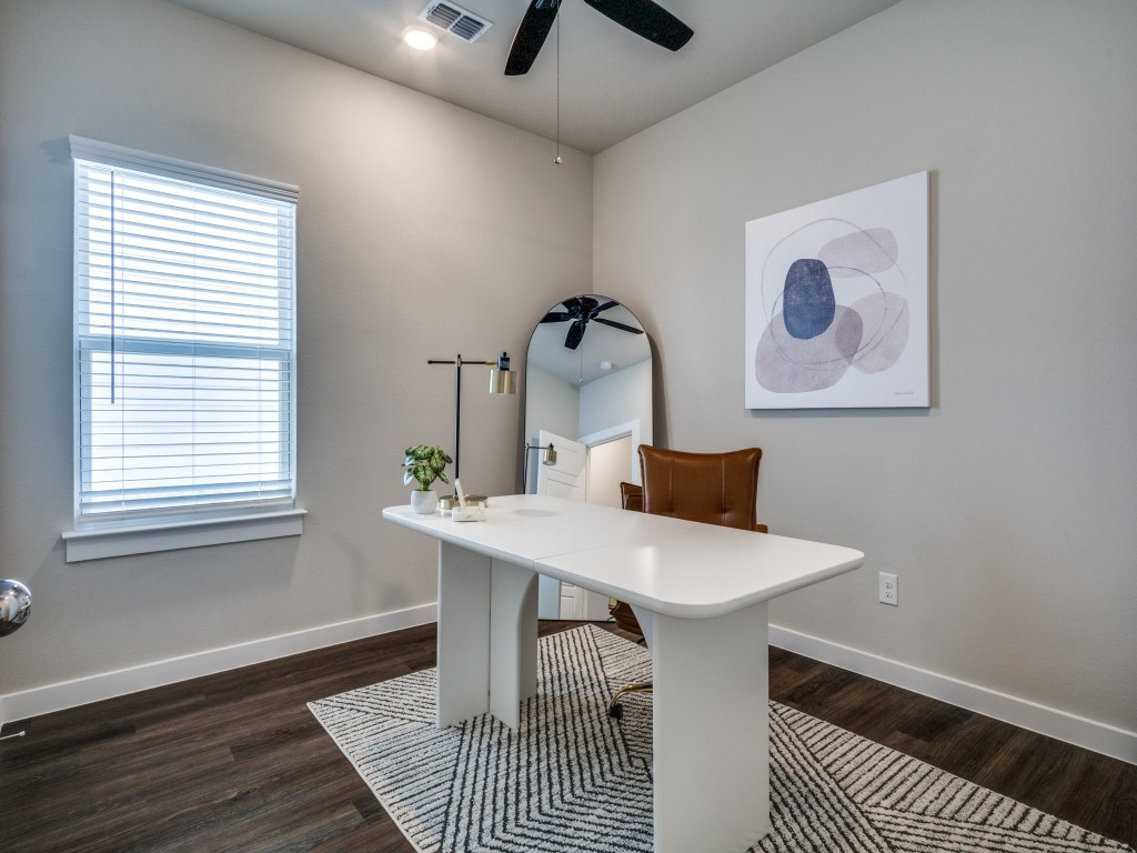 A white table with a brown chair and a mirror in a room with a ceiling fan.