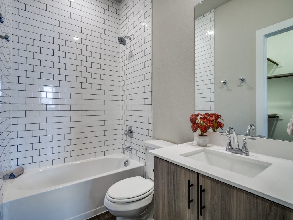 A white toilet sits next to a bathtub in a bathroom with white tiles.
