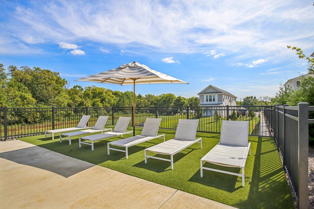 A patio with white chairs and a striped umbrella.
