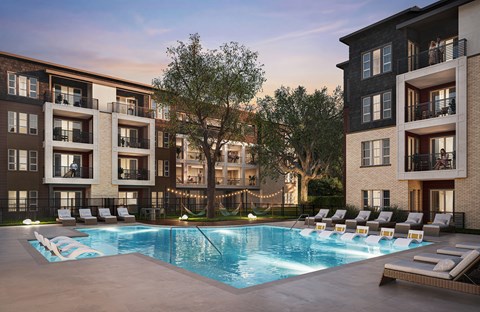 A large swimming pool surrounded by lounge chairs in front of apartment buildings.