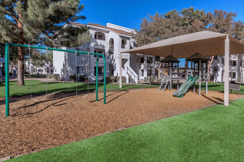 a playground with a slide and swings in front of a building