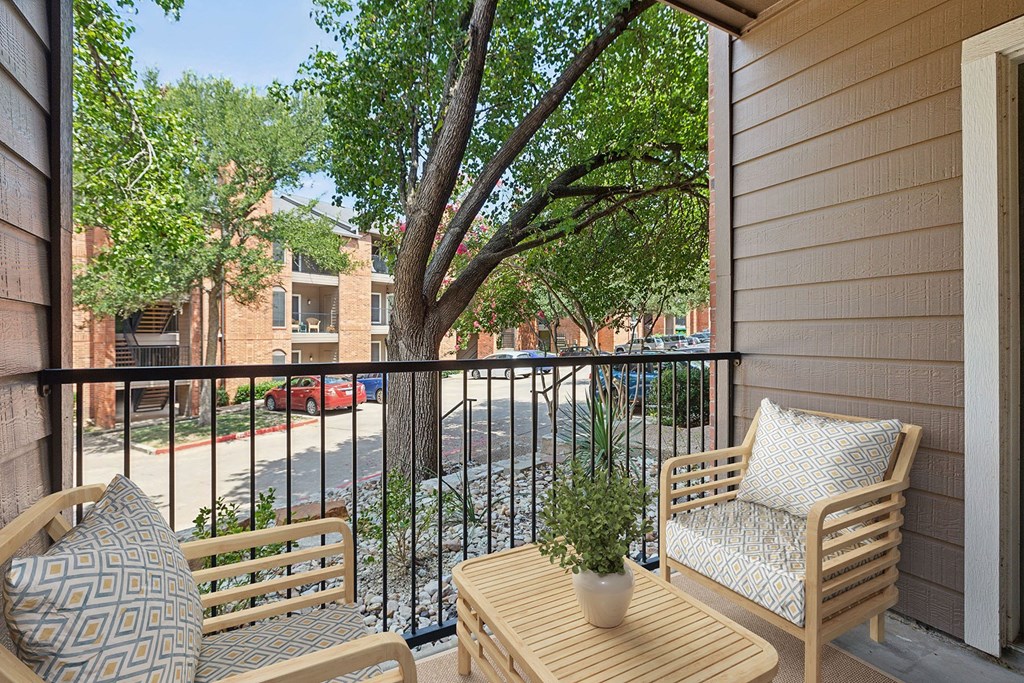 A balcony with a chair, a cushion, a table and a potted plant.
