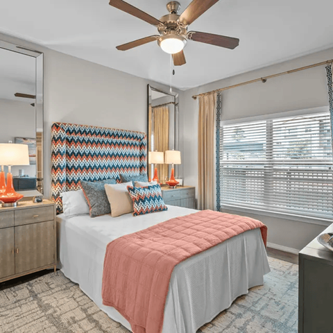 A bedroom with a bed, a ceiling fan, and a dresser with a mirror.