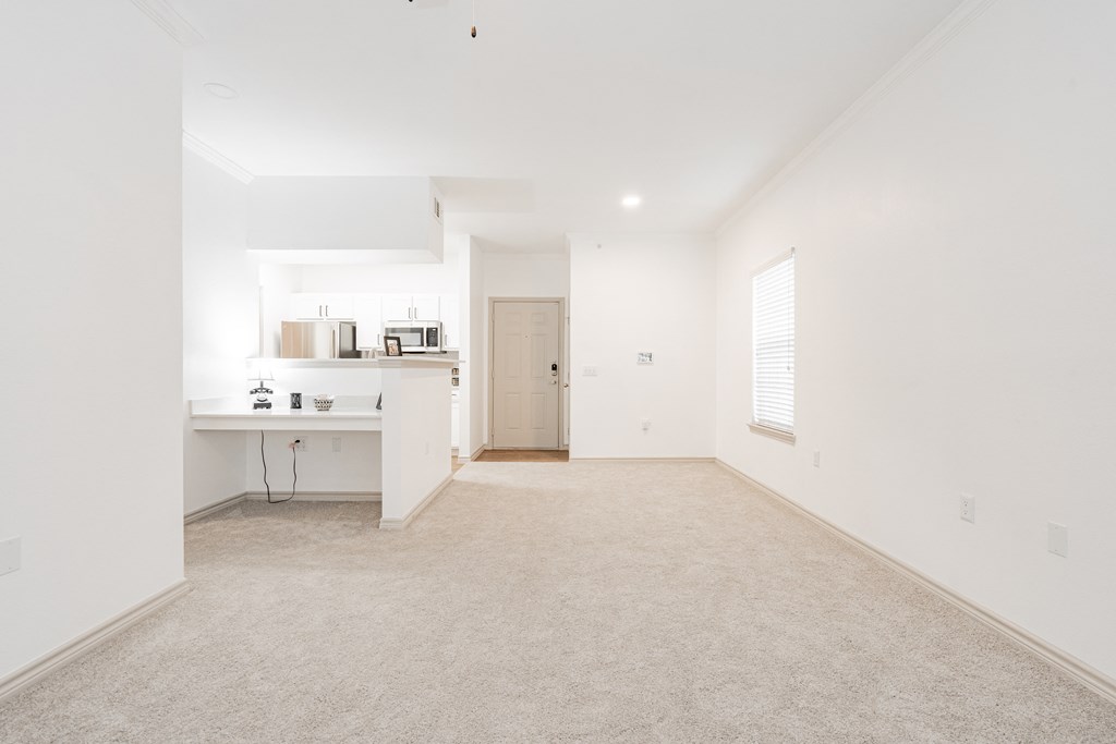 an empty living room and kitchen with white walls and carpet