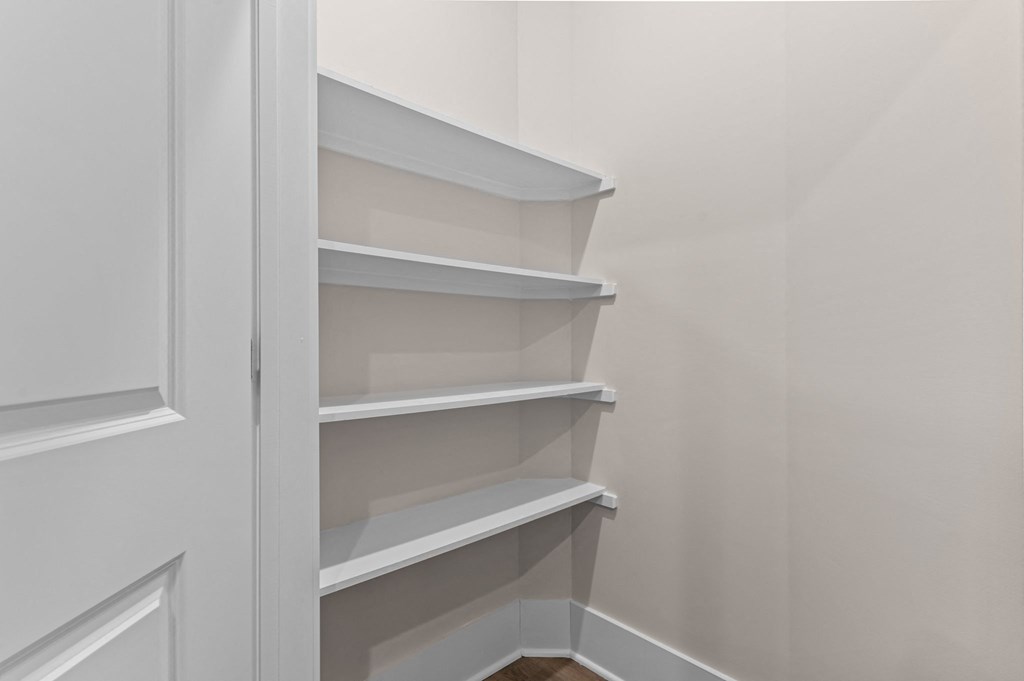 the closet in a small room with white shelves and a door