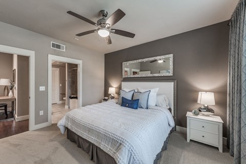 A bedroom with a large bed, a ceiling fan, and a mirror above the bed.