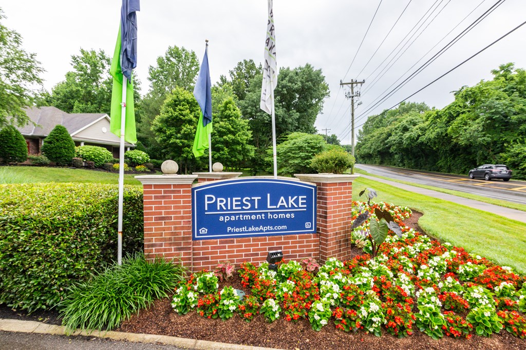 a brick monument sign with a blue and white sign on top and red and white flowers in