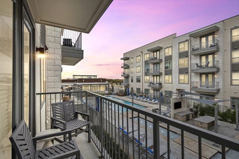 A balcony with chairs and a table overlooks a pool and buildings.