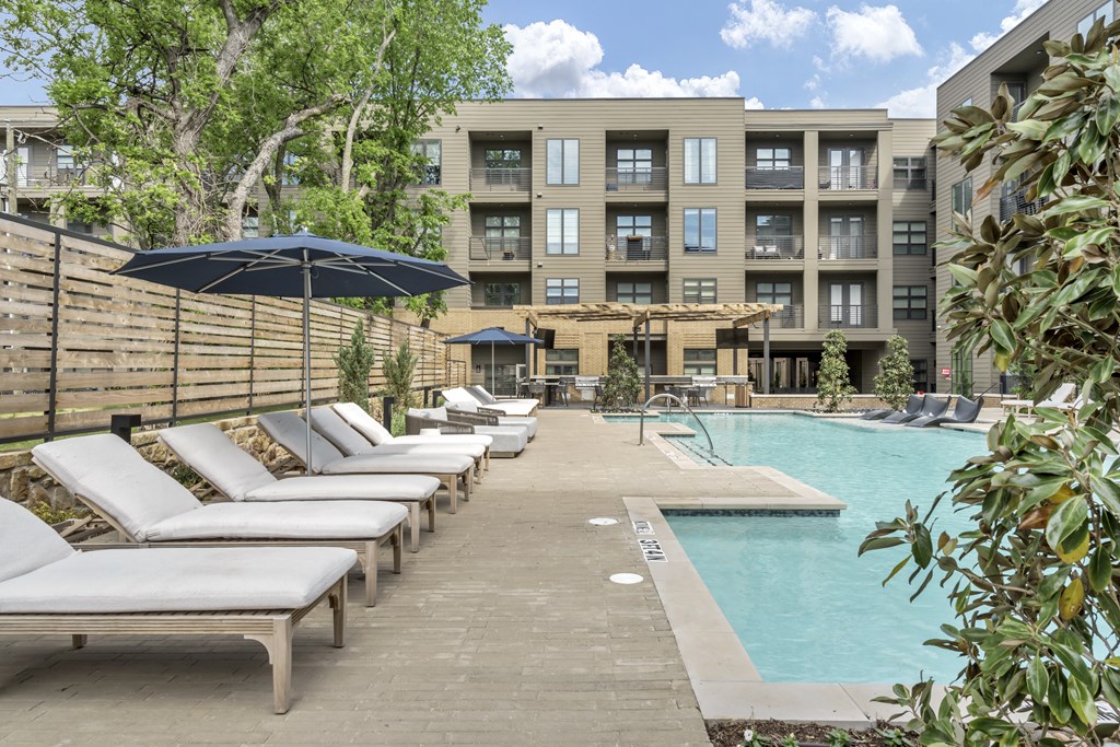 A pool area with sun loungers and a building in the background.