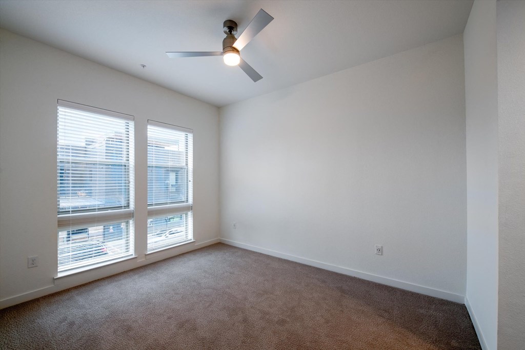 an empty living room with two windows and a ceiling fan