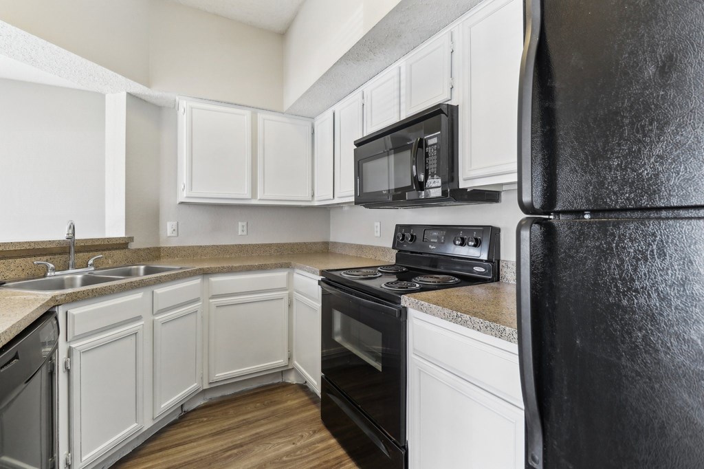 A black refrigerator is in a kitchen with white cabinets.