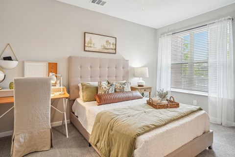 A bedroom with a bed, desk, chair, and window.