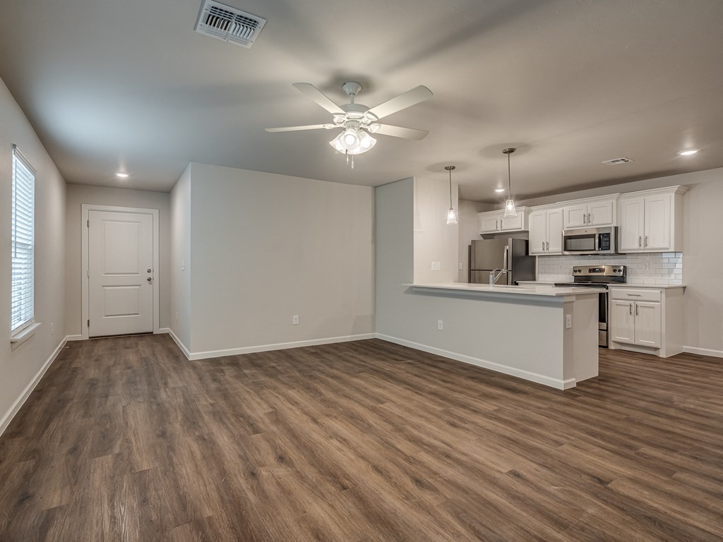 an empty living room with a kitchen in the background
