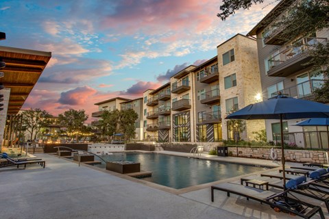 A swimming pool surrounded by lounge chairs and umbrellas in front of a modern apartment building.