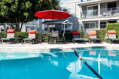 A pool with chairs and an umbrella in front of a building.
