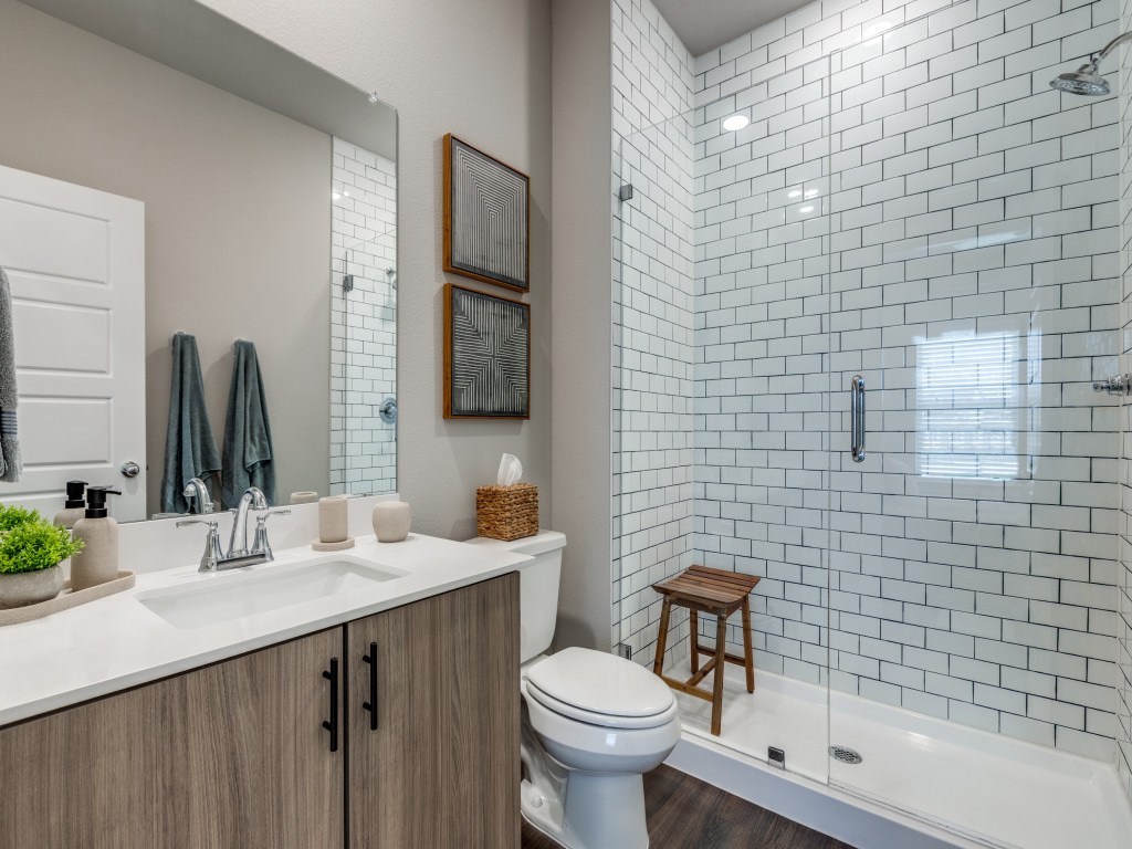 A white toilet sits in a bathroom with a white tiled shower.