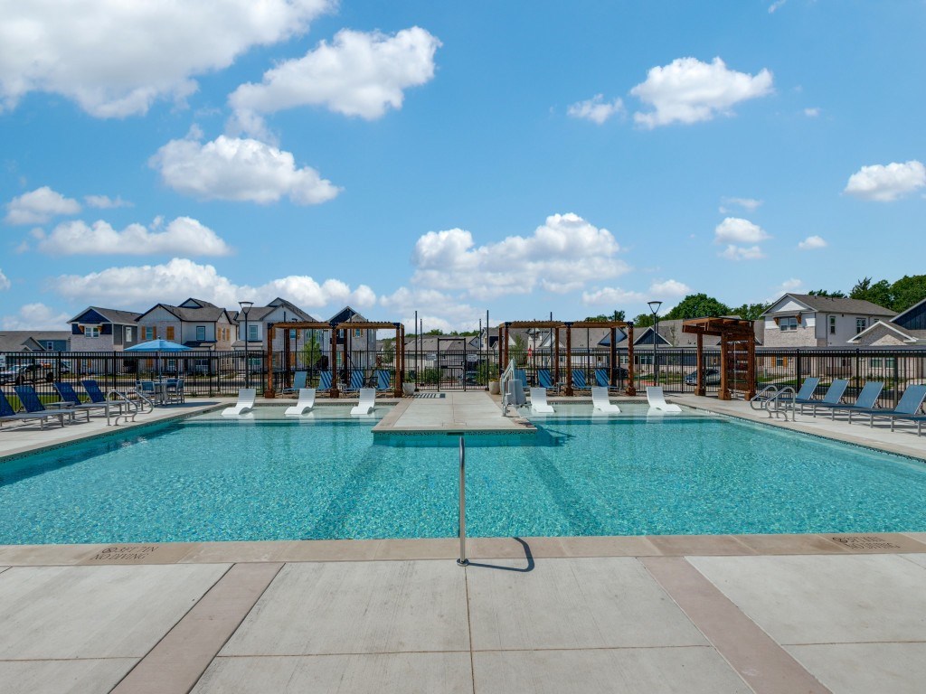 A large swimming pool with a fountain in the middle and lounge chairs around it.