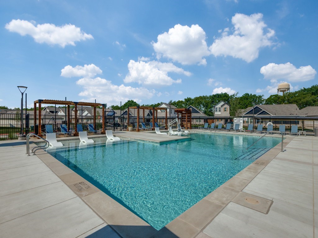 A large swimming pool with a blue tinted water and white chairs around it.