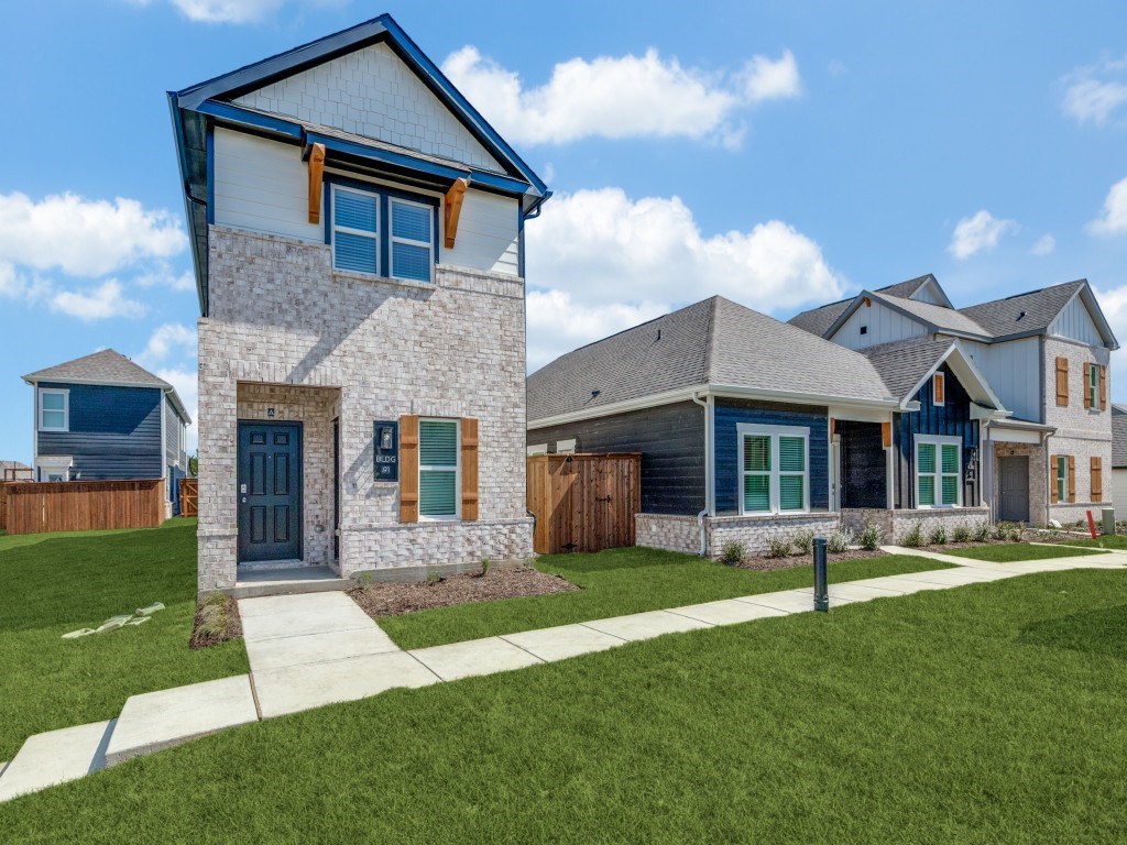 A house with a blue door and windows is surrounded by a grassy area and other houses.