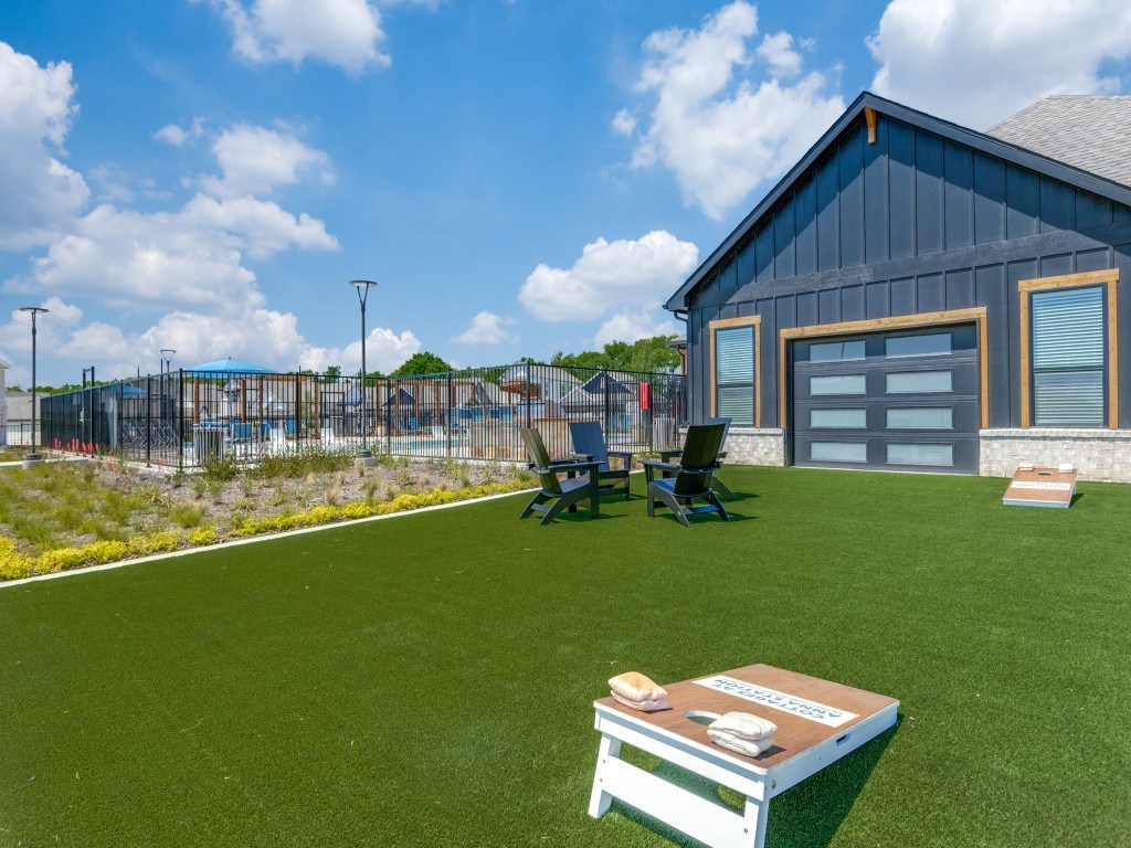 A wooden picnic table sits on a green lawn in front of a house.