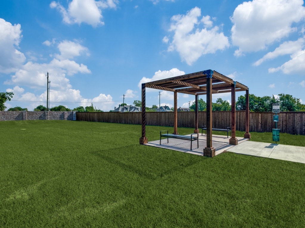 A wooden pavilion with a bench is situated in a grassy area.