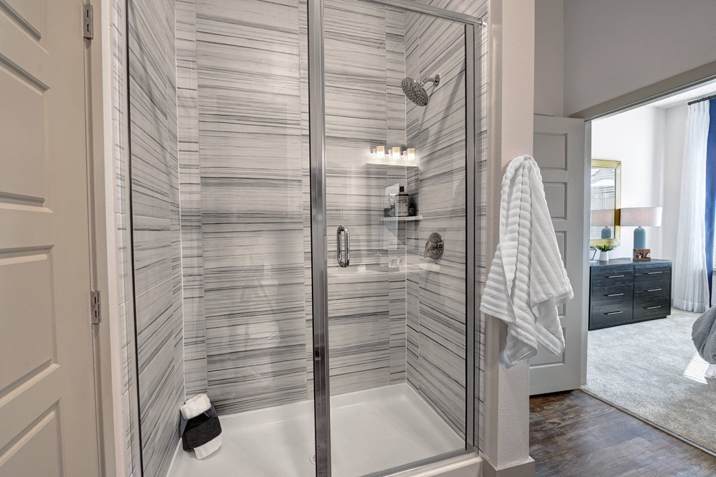 A modern bathroom with a glass shower enclosure and a white towel hanging on the door.