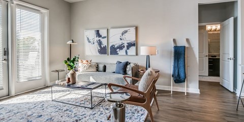 A modern living room with a glass coffee table and a large abstract painting on the wall.