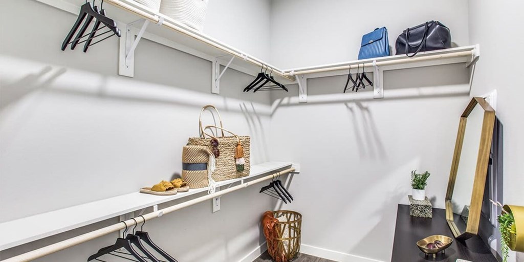 A white closet with clothes hanging and a mirror on the right.