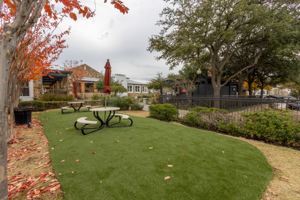 a picnic area with a table and umbrella in the middle of a grassy area
